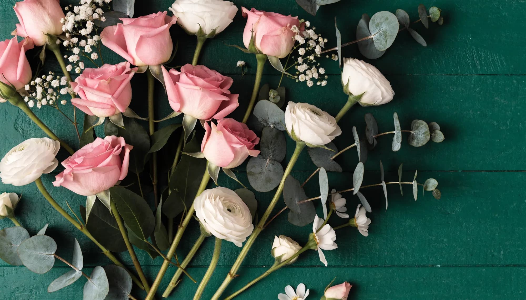 Rosa Rosen, weiße Ranunkeln und Eukalyptuszweige auf dunkelgrünem Holz